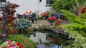 Um jardim com lago, área de estar externa e plantas em vasos.