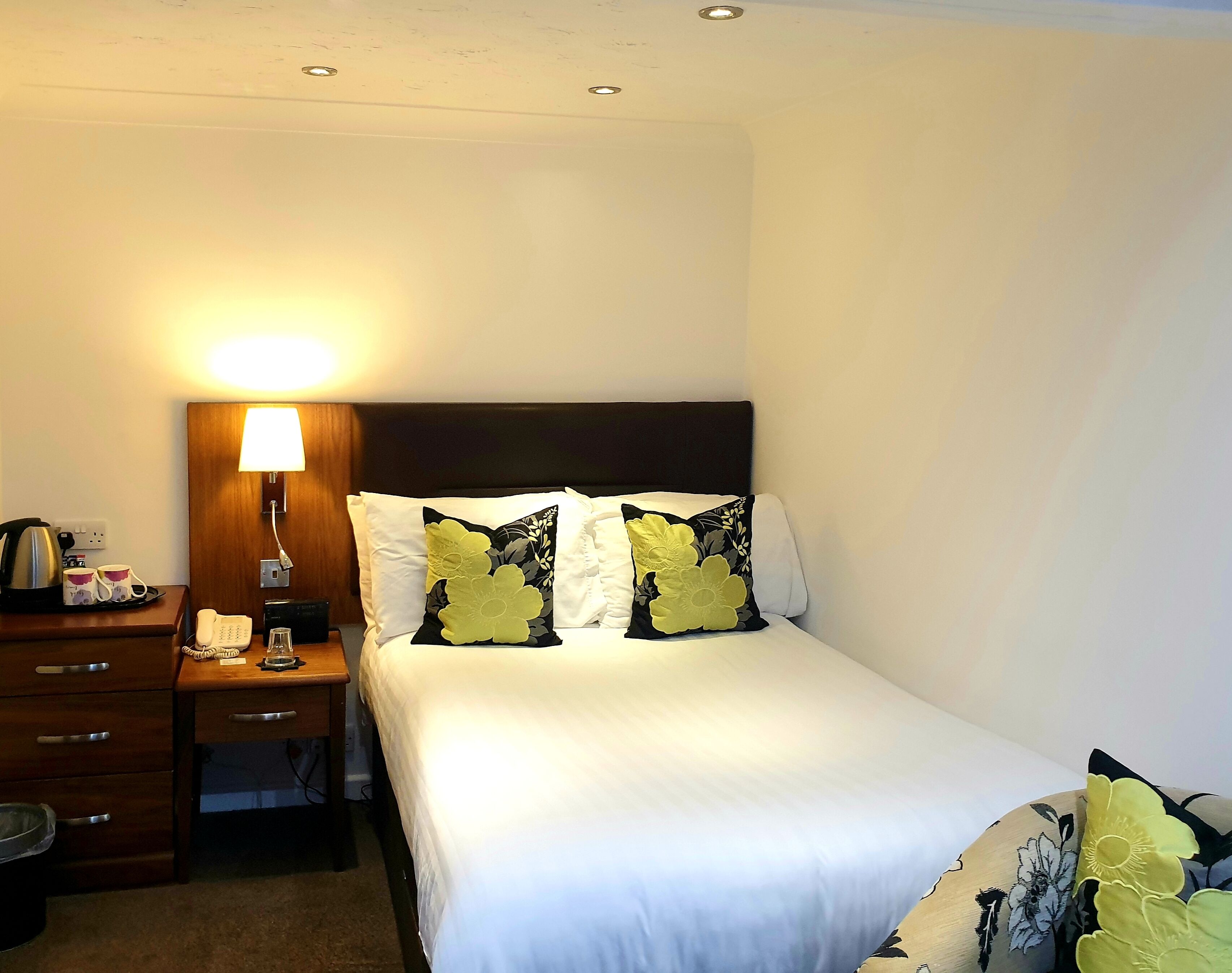 A hotel room with a bed, a bedside table with a lamp, a telephone, and a trash bin.