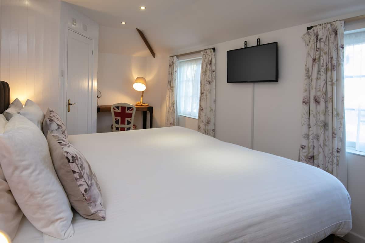 A bedroom with a large bed, a desk with a lamp, a flat-screen TV, and floral curtains.
