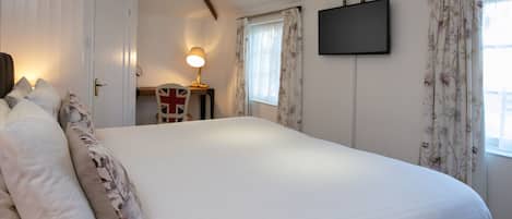 Ein Schlafzimmer mit einem großen Bett, einem Schreibtisch mit Lampe, einem Flachbildfernseher und floralen Vorhängen.