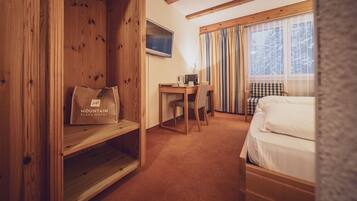 A hotel room with a wooden desk, a bed, a chair, and a window with curtains.