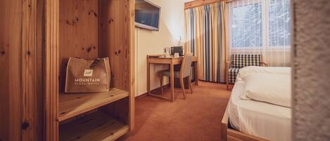 Une chambre d’hôtel avec un bureau en bois, un lit, une chaise et une fenêtre avec des rideaux.