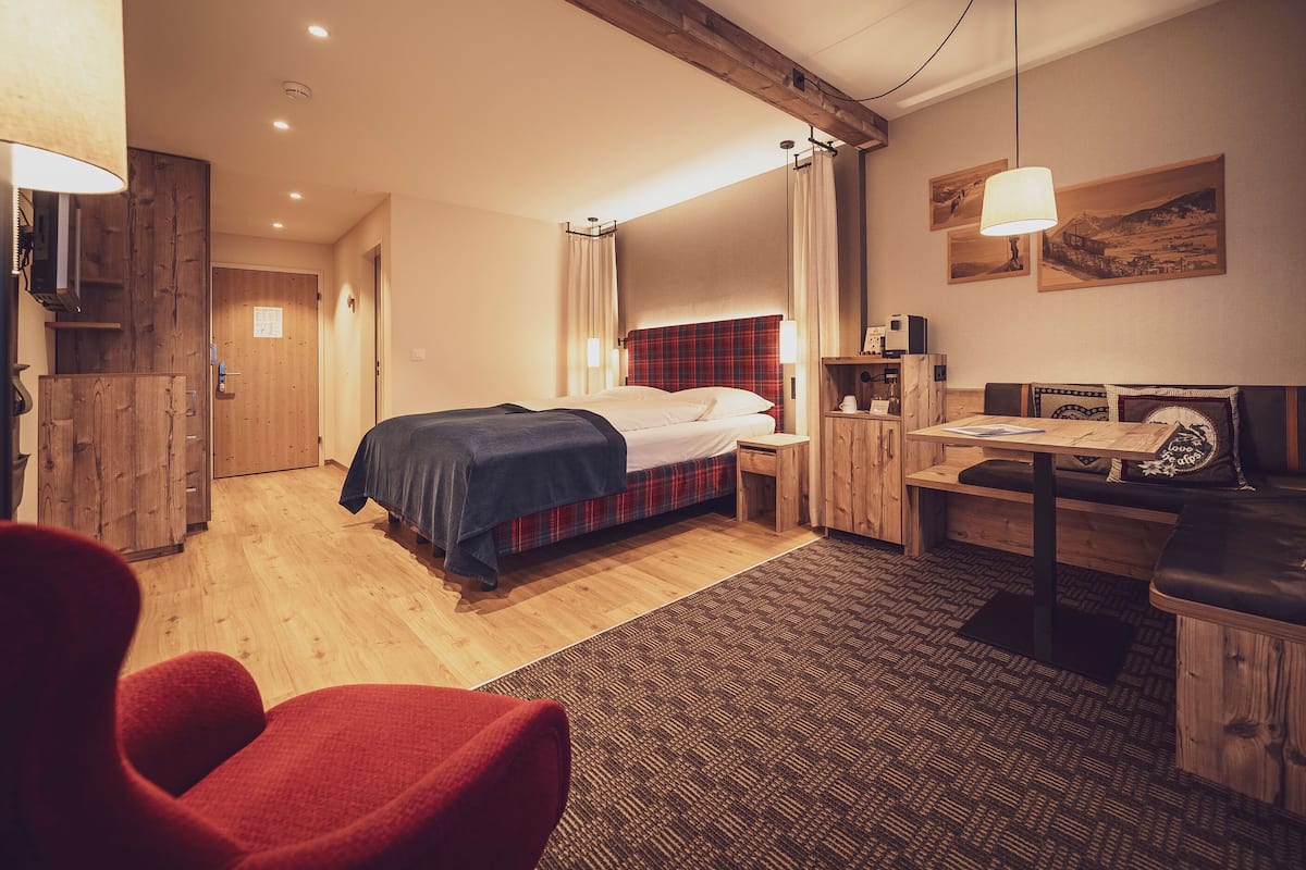 Ein gemütliches Hotelzimmer mit einem Bett, einem Schreibtisch, einem Sessel und einem kleinen Tisch.