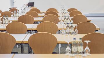 Un salón de conferencias con filas de mesas y sillas de madera, equipado con botellas de agua y copas de vino.