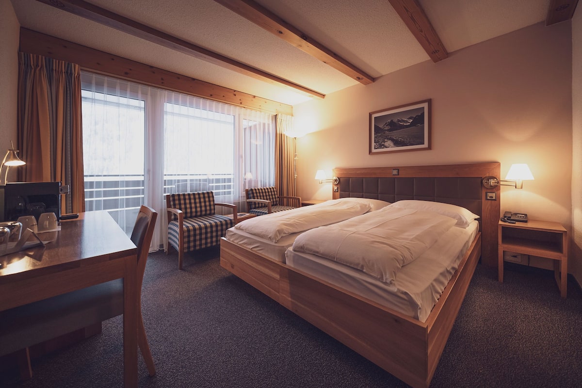 Ein Hotelzimmer mit Doppelbett, Schreibtisch mit Stuhl, einem kleinen Tisch und einer Lampe.