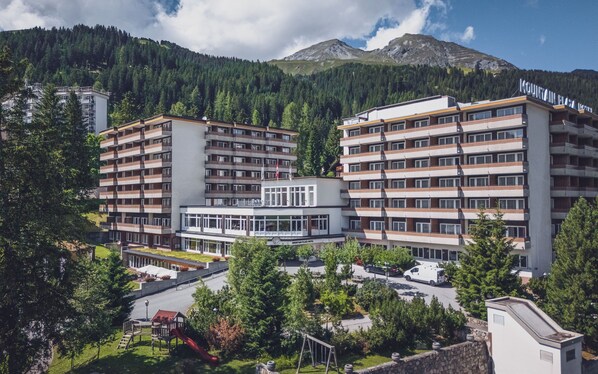 A hotel with multiple floors, a central lobby, and a mountainous backdrop. - Mountain Plaza Hotel (Davos)