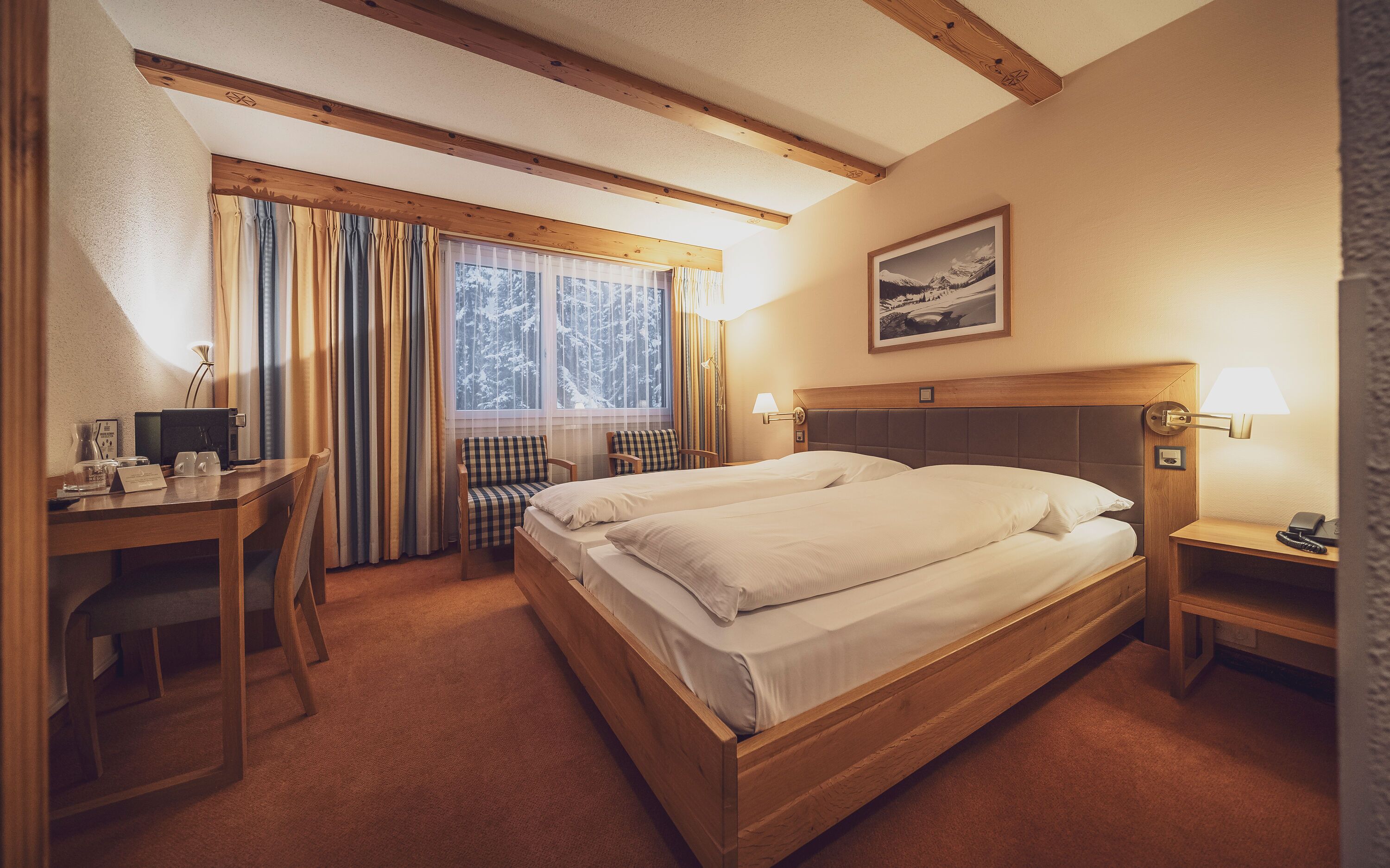 Una habitación de hotel con una cama grande, un escritorio con silla, una mesita y una ventana con cortinas.