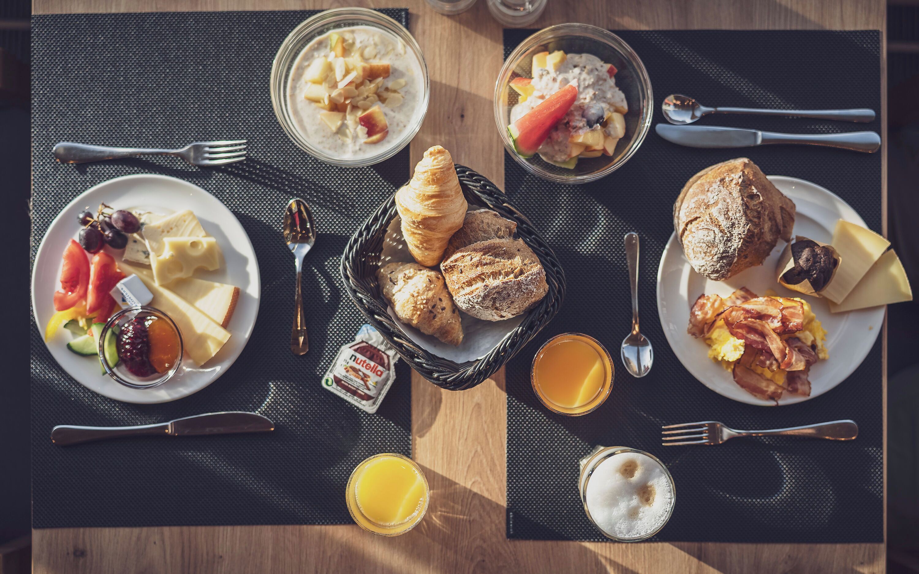 Desayuno con platos de comida, una cesta de pan y un vaso de zumo de naranja.