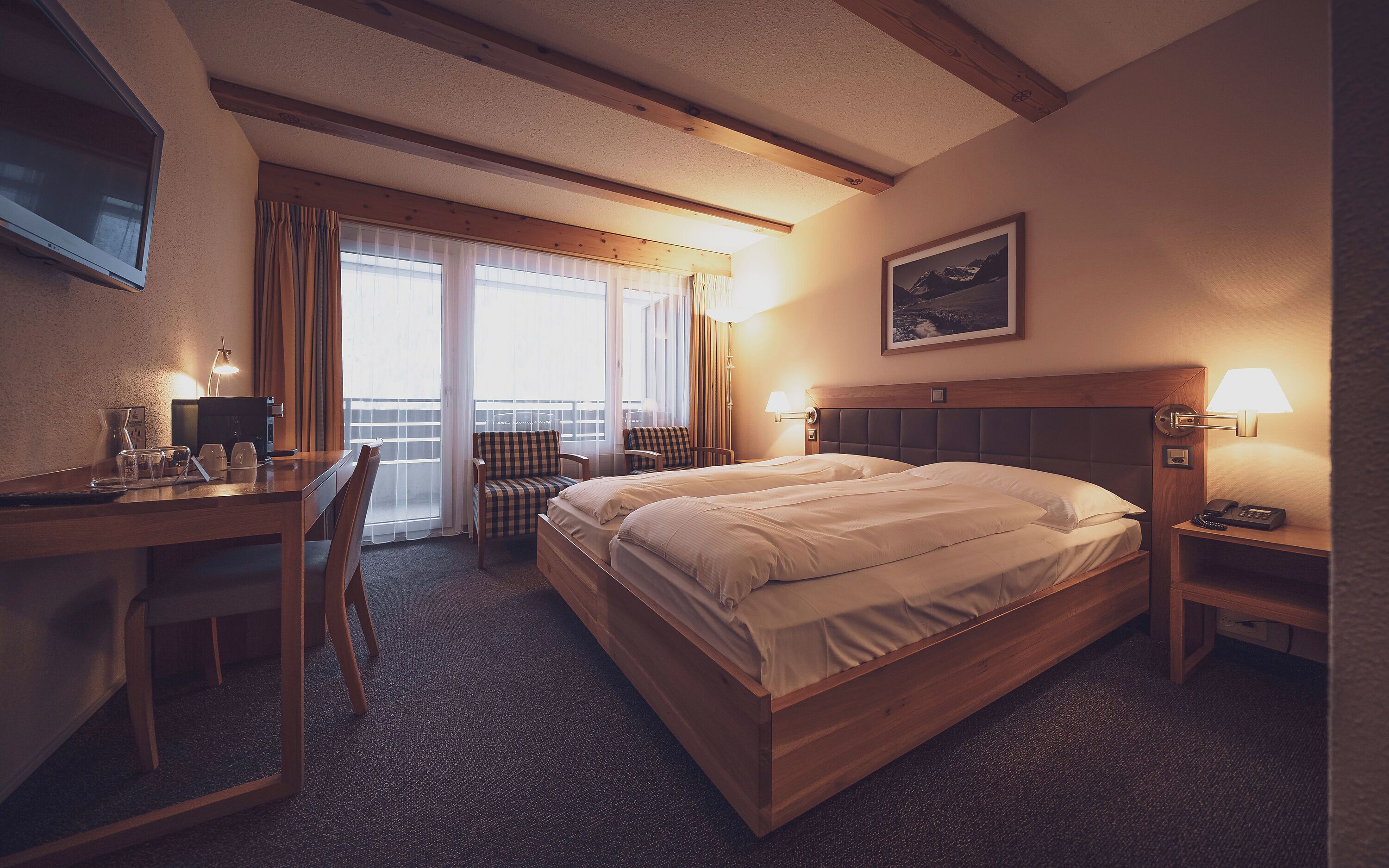 A hotel room with a bed, desk, chair, and a window with curtains.