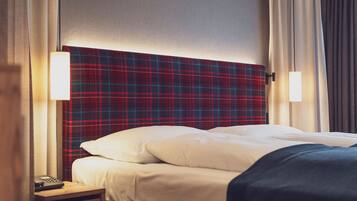 Una habitación de hotel con cabecera a cuadros, una mesita de noche con control remoto y una cama con ropa blanca.