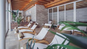 A sunlit indoor relaxation area with wooden ceiling beams, stone walls, and white cushioned lounge chairs. - Mountain Plaza Hotel (Davos)