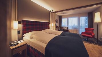 A hotel room with a bed, bedside table, lamp, chair, and a view of the outdoors.