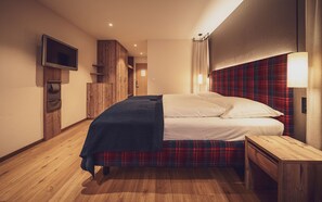 A hotel room with a bed, a wooden nightstand, a TV mounted on the wall, and a plaid-patterned headboard. - Mountain Plaza Hotel (Davos)