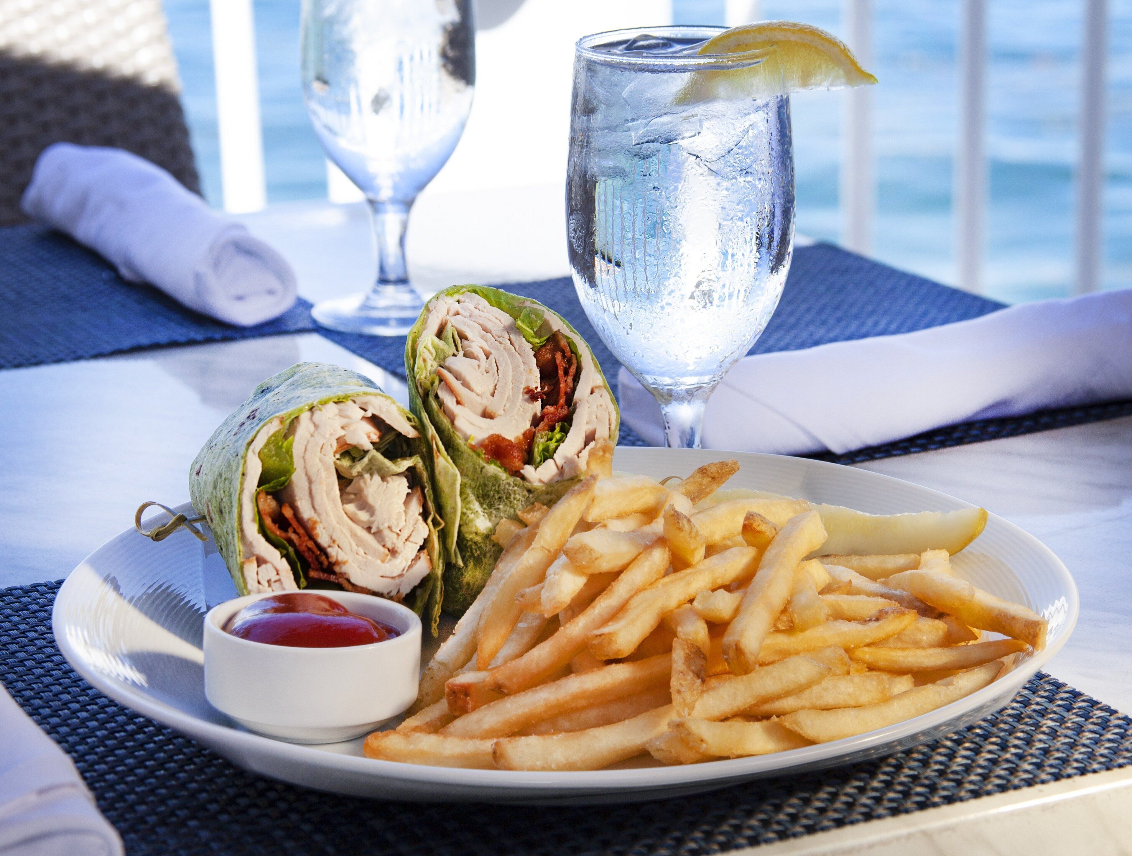 A plate with a wrap sandwich, a glass of water, and a side of French fries.