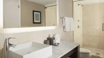A modern bathroom with a large mirror, a white sink, a shower, and a toilet.