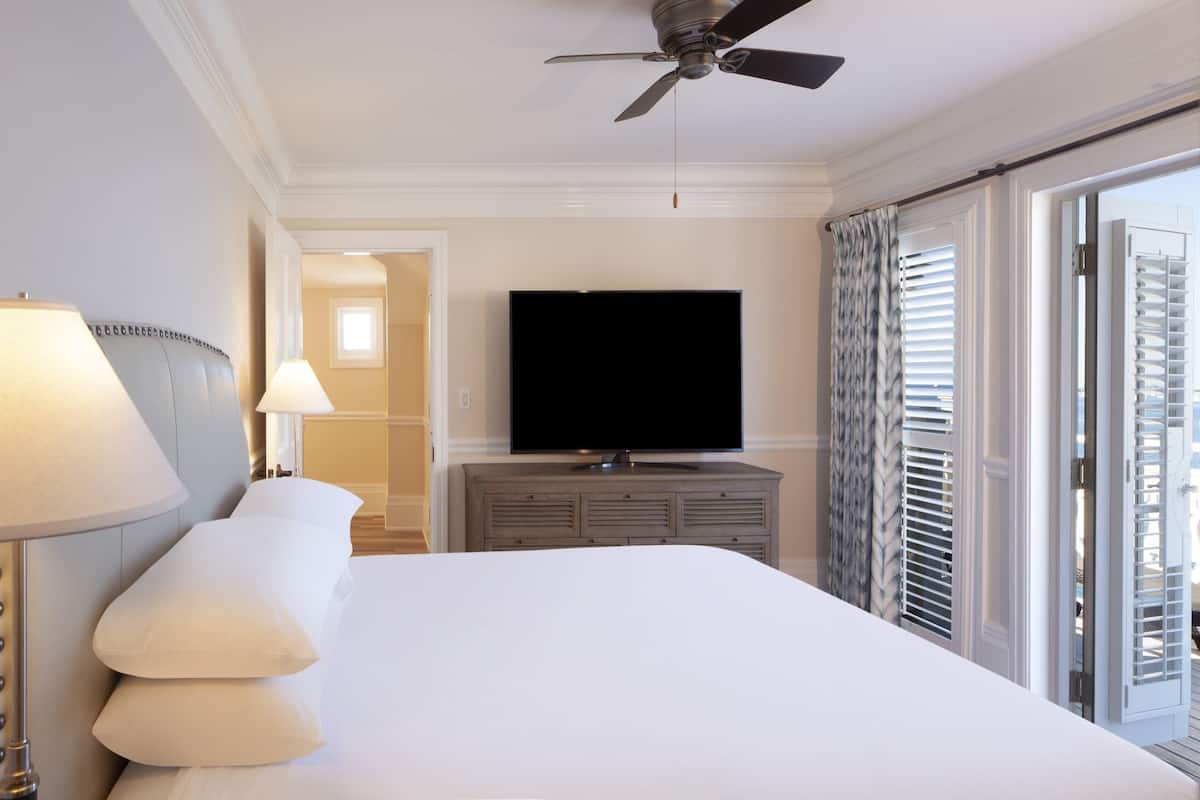 A hotel room with a large bed, a flat-screen TV, a ceiling fan, and a view of the city through the window.