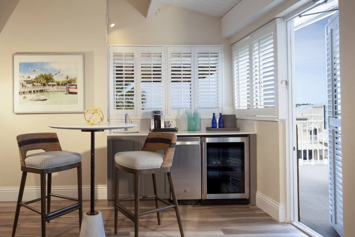 A modern kitchen with a dining area, featuring a kitchen island, bar stools, a refrigerator, and a view through the window.