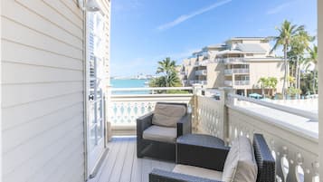 Un balcon agrémenté de meubles en osier, une vue sur l’océan et un immeuble doté de balcons et de palmiers.