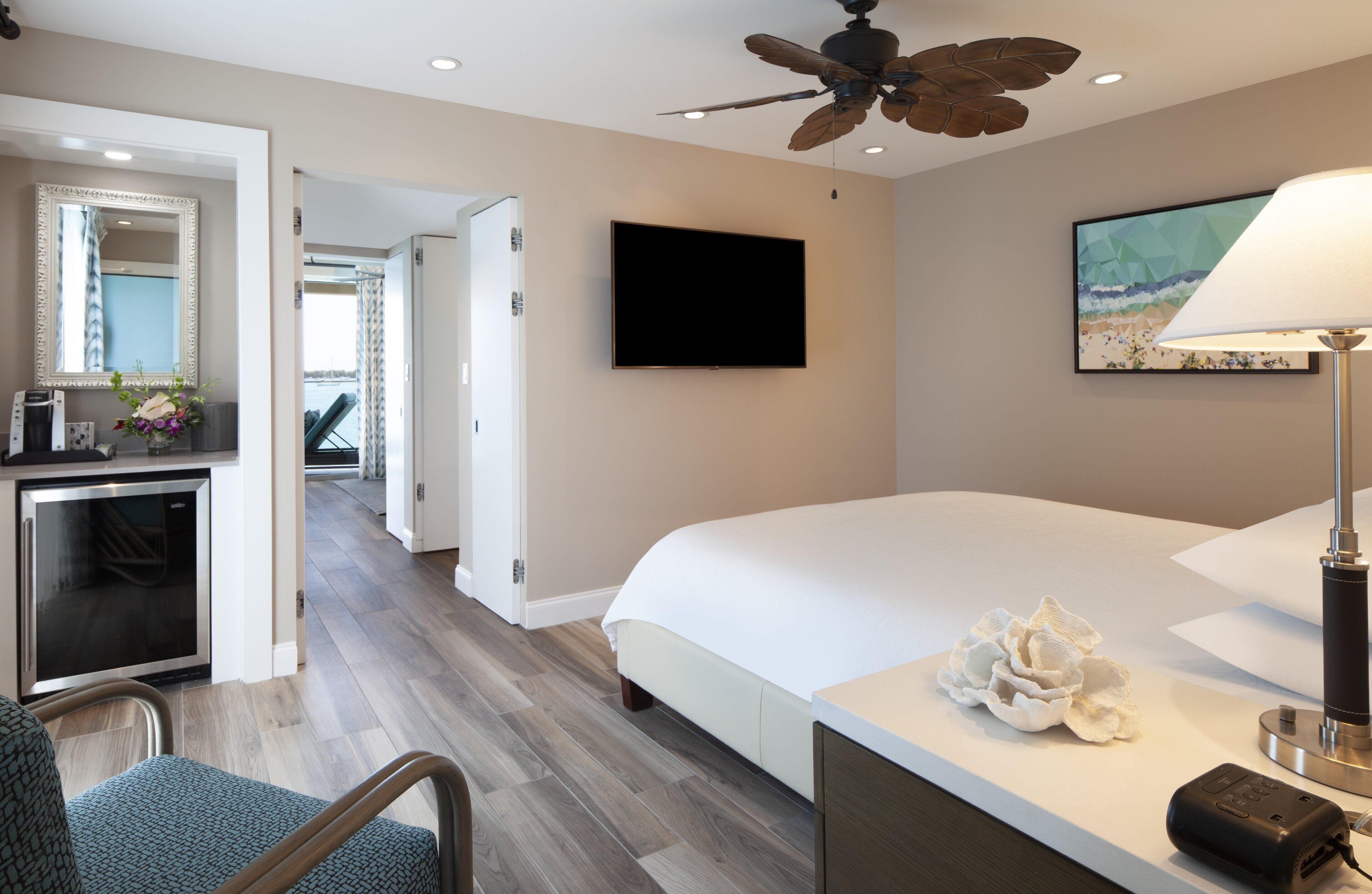 A hotel room with a bed, a desk with a computer, a television, and a ceiling fan.