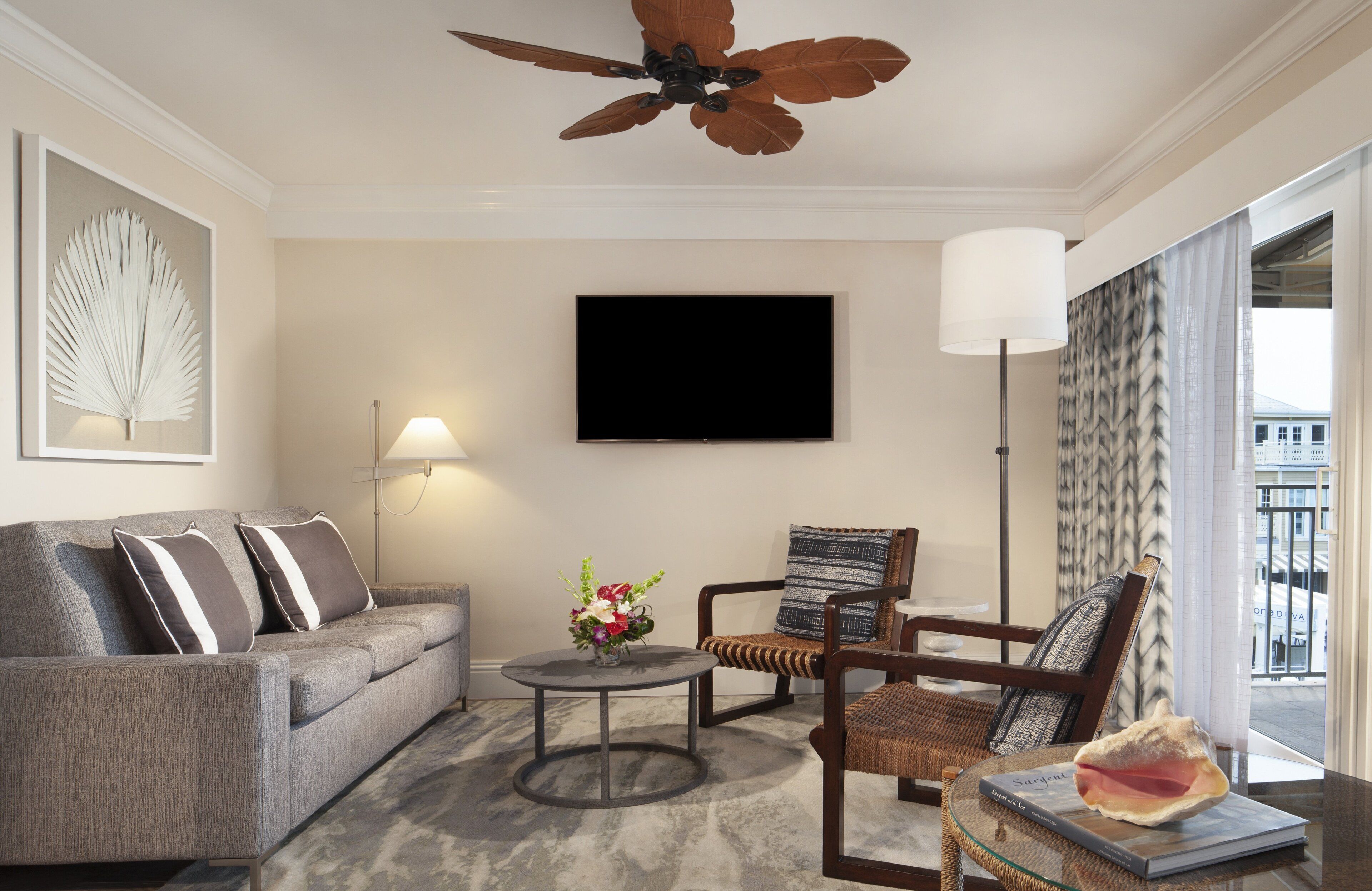 A modern living room with a grey sofa, a round coffee table, a wicker chair, and a ceiling fan.