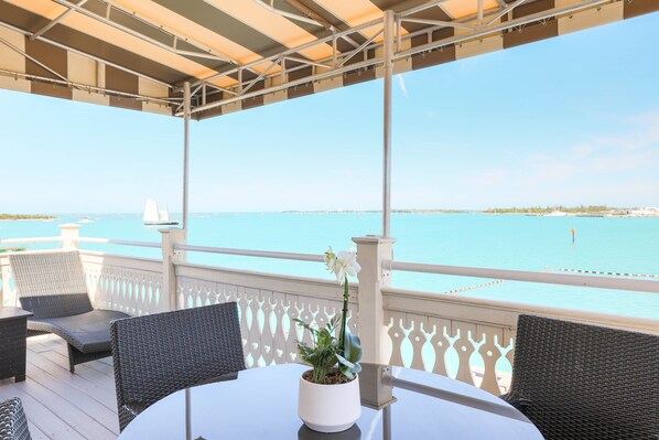 A covered outdoor seating area with wicker chairs and a table, overlooking a calm sea.