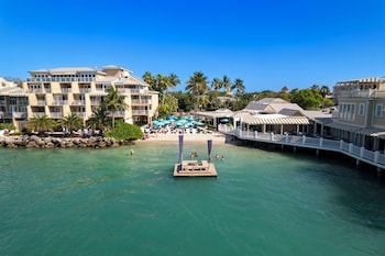 A pool area with lounge chairs and umbrellas, surrounded by palm trees and a building with balconies. at Pier House Resort & Spa