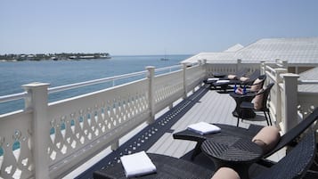 A deck with lounge chairs and a white railing overlooking the sea.