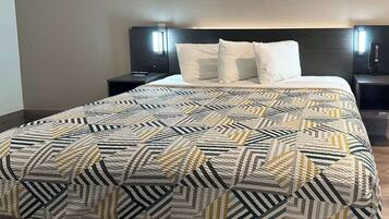 A hotel room with a bed, a nightstand, a wall-mounted lamp, and a bedside table.