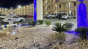 Entrada de hotel con fuente, piedras y estacionamiento.
