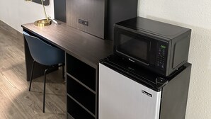 Una kitchenette compacta con microondas, refrigerador y un pequeño comedor con una silla y un escritorio.