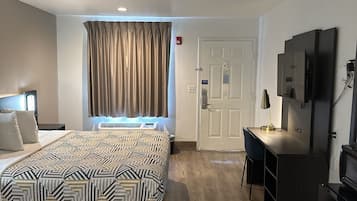A hotel room with a bed, a desk, a TV, and a door.