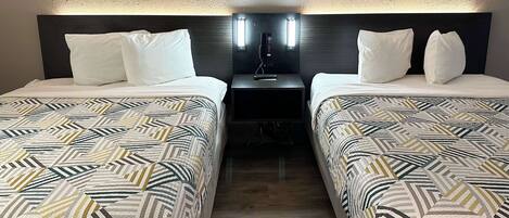 Habitación de hotel con dos camas, cada una con ropa de cama estampada, una mesita de noche con lámpara y un aplique en la pared.