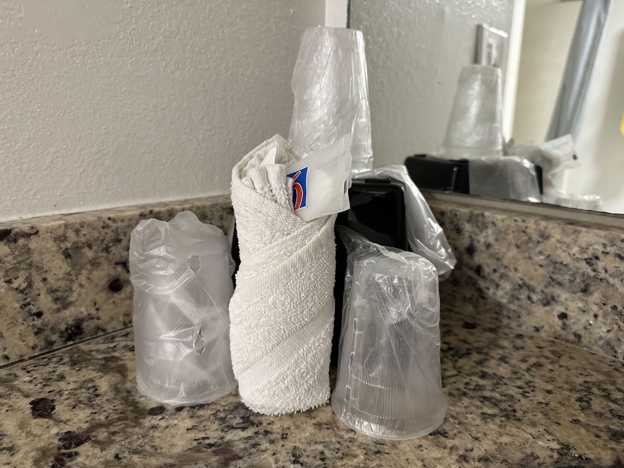 Un baño con encimera de granito, una toalla blanca y artículos envueltos en plástico.