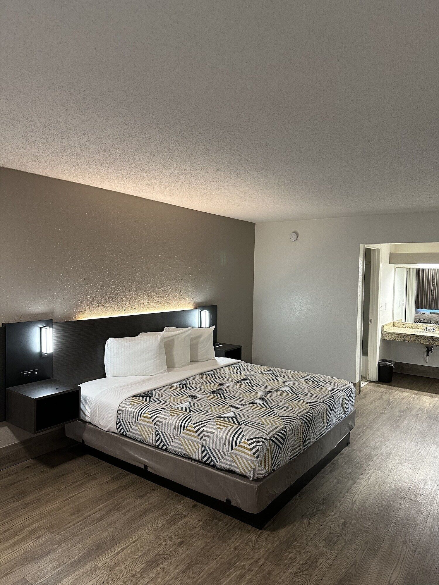 Een moderne hotelkamer met een groot bed, een nachtkastje, een wandlamp en een houten vloer.