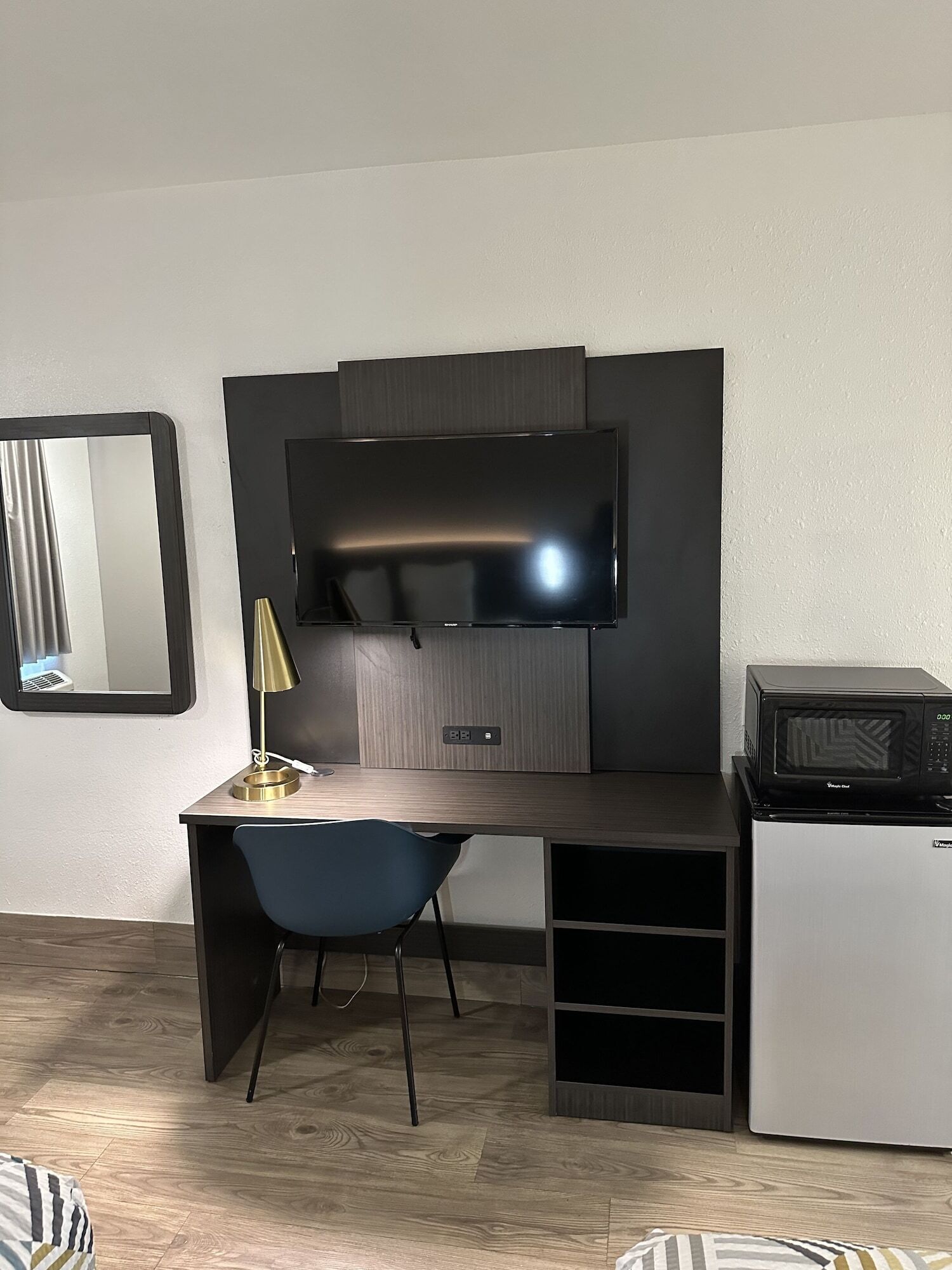 A modern room with a flat-screen TV mounted on a dark wall, a small desk with a chair, and a microwave on a small table.