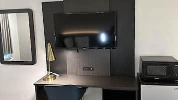 Una habitación moderna con un televisor de pantalla plana montado en una pared oscura, un escritorio pequeño con una silla y un microondas sobre una mesita.
