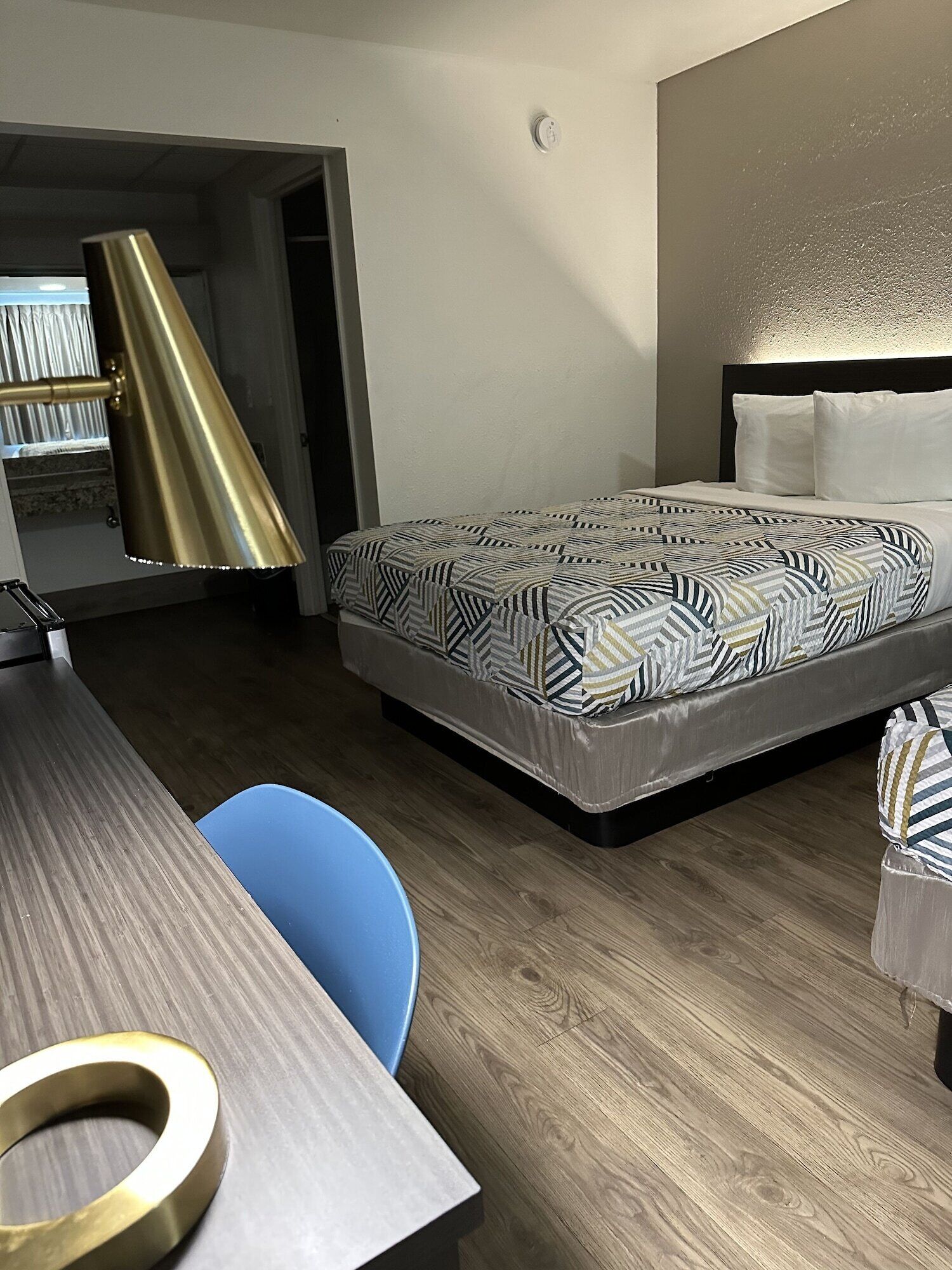 A hotel room with a bed, a desk, a chair, and a bookshelf.