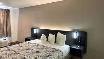 A hotel room with a large bed, two bedside tables, a headboard with integrated lighting, a window with curtains, and a wall-mounted telephone.