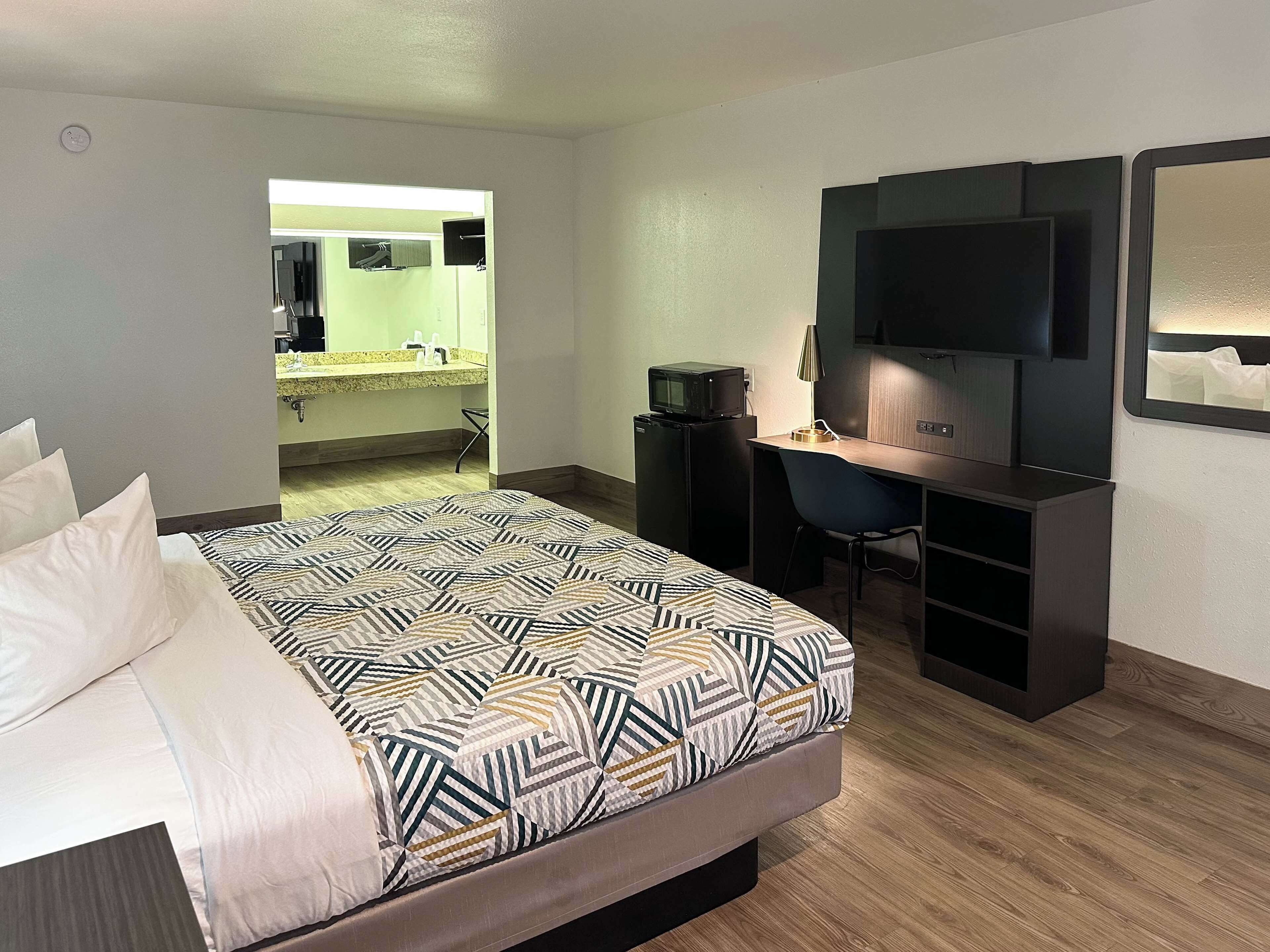 Una camera d'albergo con un letto, una scrivania, una televisione e un bagno visibile attraverso una porta aperta.