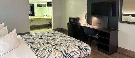 Una camera d'albergo con un letto, una scrivania, una televisione e un bagno visibile attraverso una porta aperta.