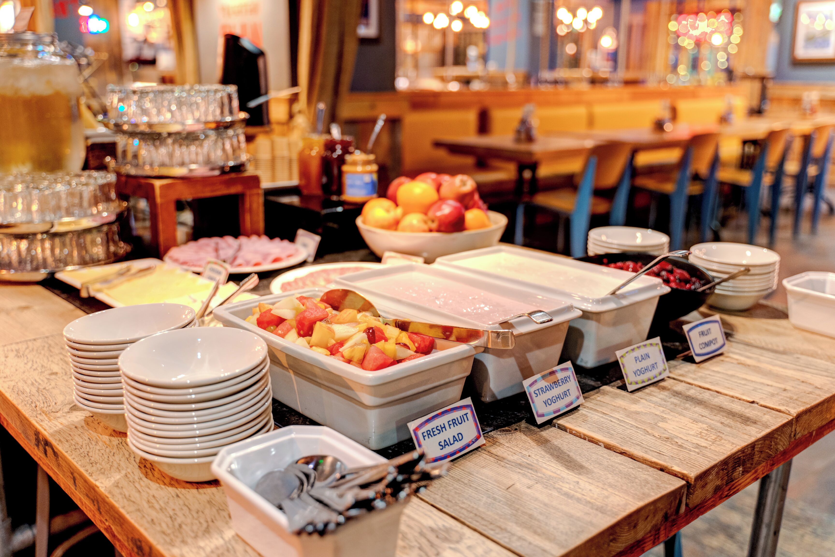 A buffet table with various food options including fresh fruit salad, plain yogurt, and fruit compote.