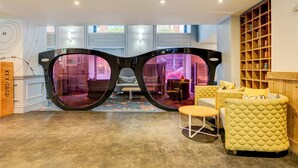 A room with a large pair of glasses-shaped mirrors, a yellow cushioned sofa, a small round table, and a wooden shelving unit.