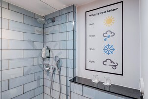 A modern bathroom with a shower, a glass shower door, and a wall-mounted weather forecast poster.