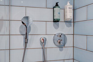 Un baño con ducha, cabezal de ducha y panel de control en la pared.