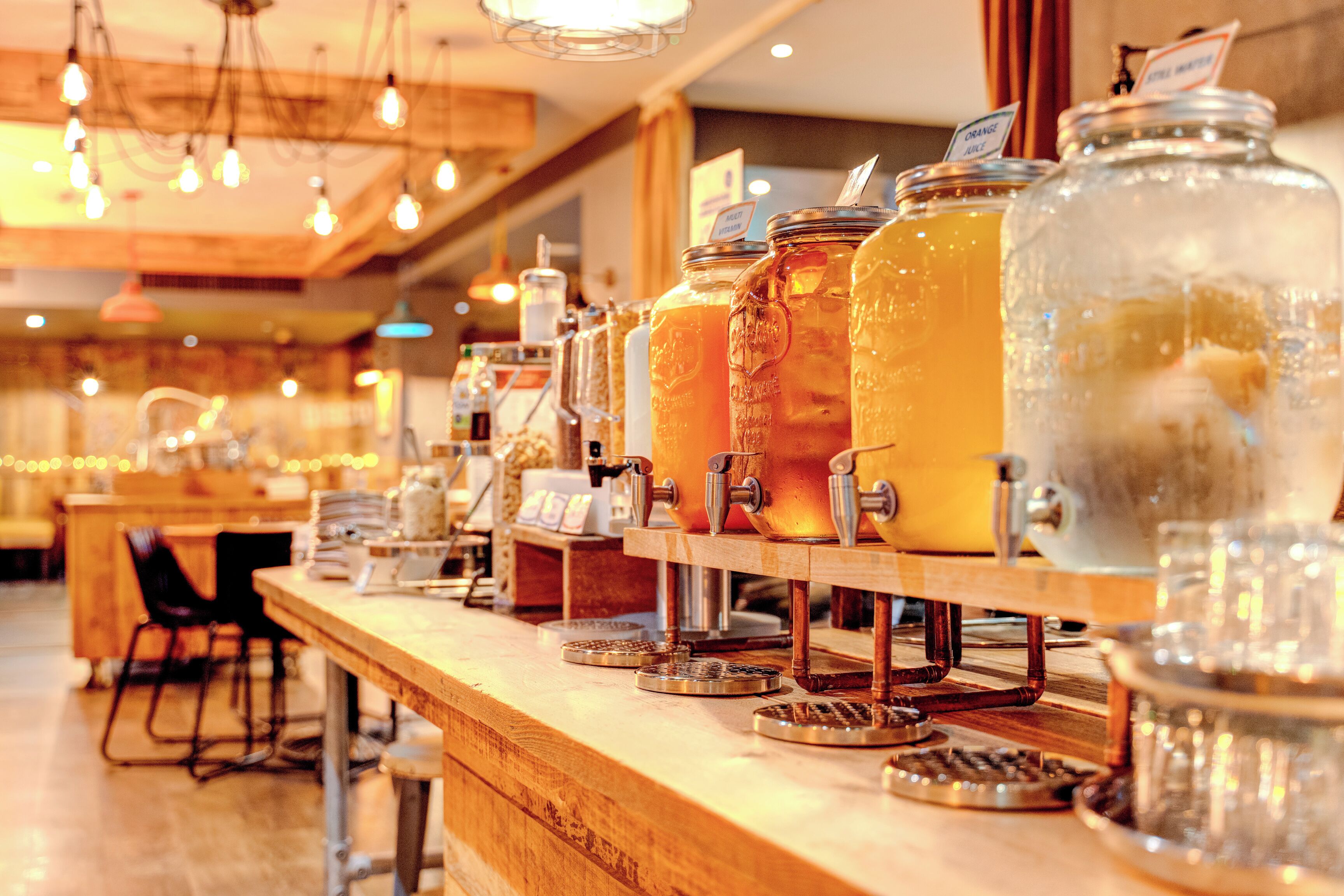 A bar area with multiple large glass jars filled with beverages, a coffee machine, and a wooden counter.