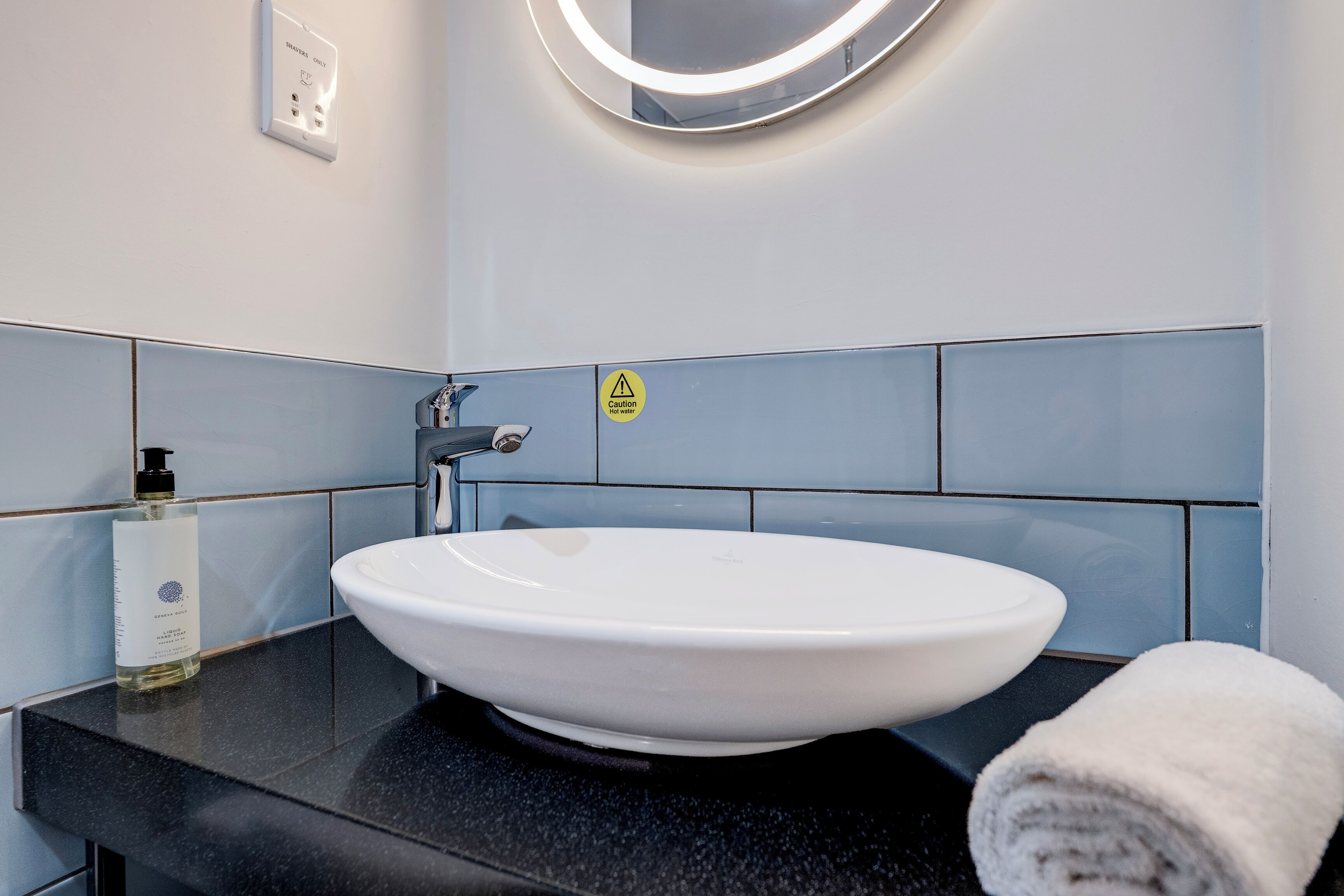 Une salle de bain avec un lavabo blanc, un plan de toilette noir et une serviette.