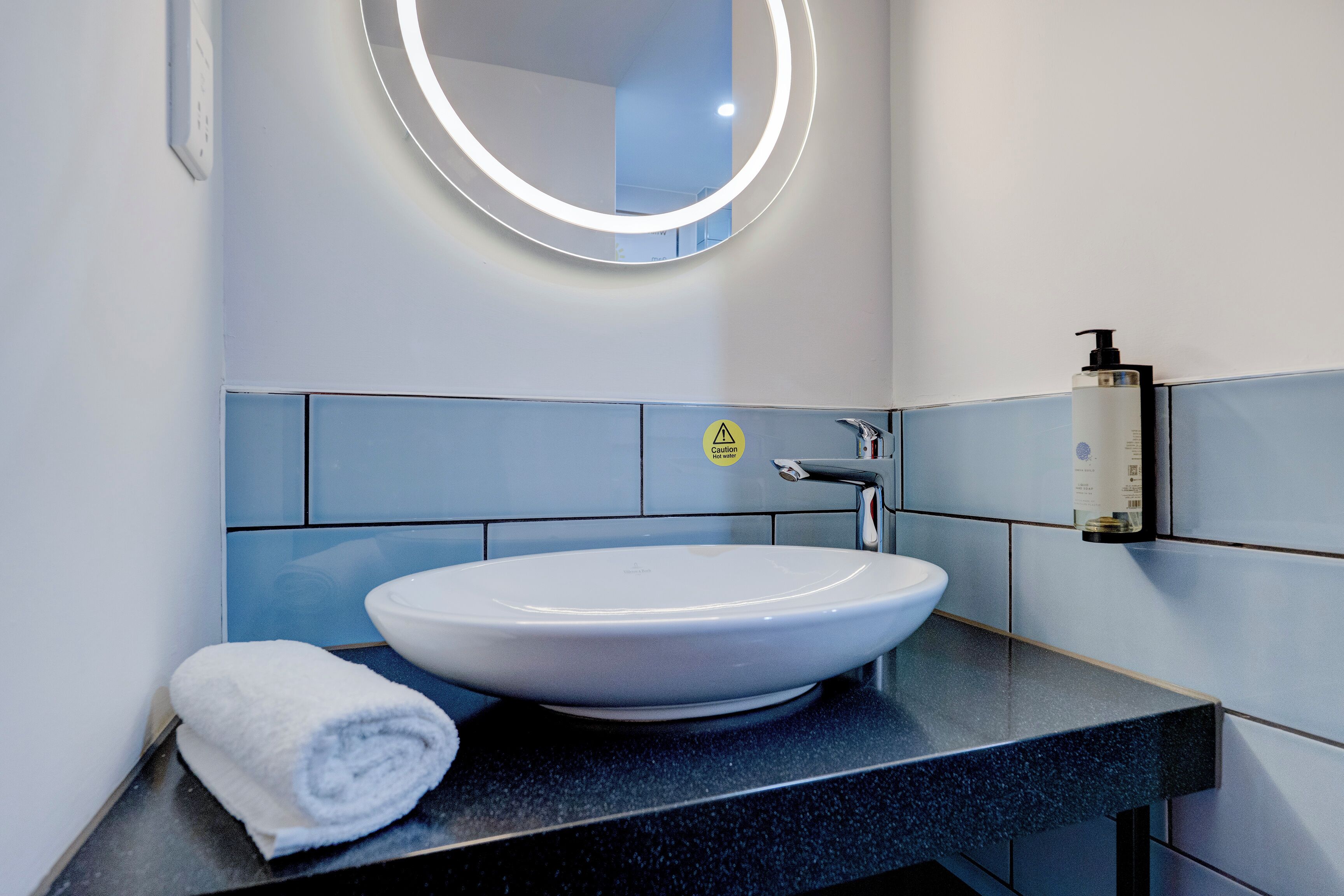 Ein modernes Badezimmer mit einem runden Spiegel, einem weißen Waschbecken und einem Handtuch auf der Ablagefläche.