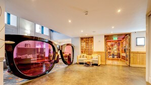 A spacious lobby with a large mirror, a seating area with a sofa and armchairs, and a view into a restaurant or dining area.