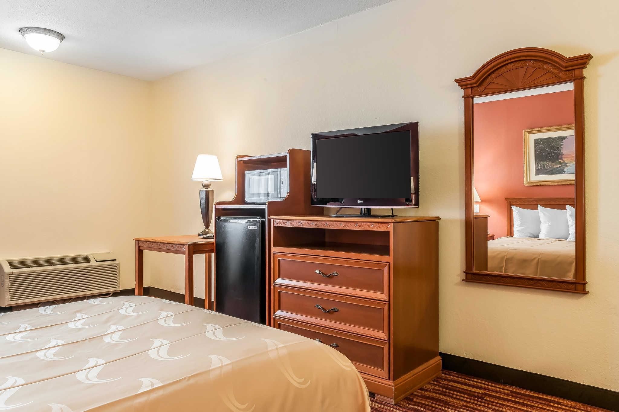 A hotel room with a bed, a television, a dresser, a mirror, and a heater.