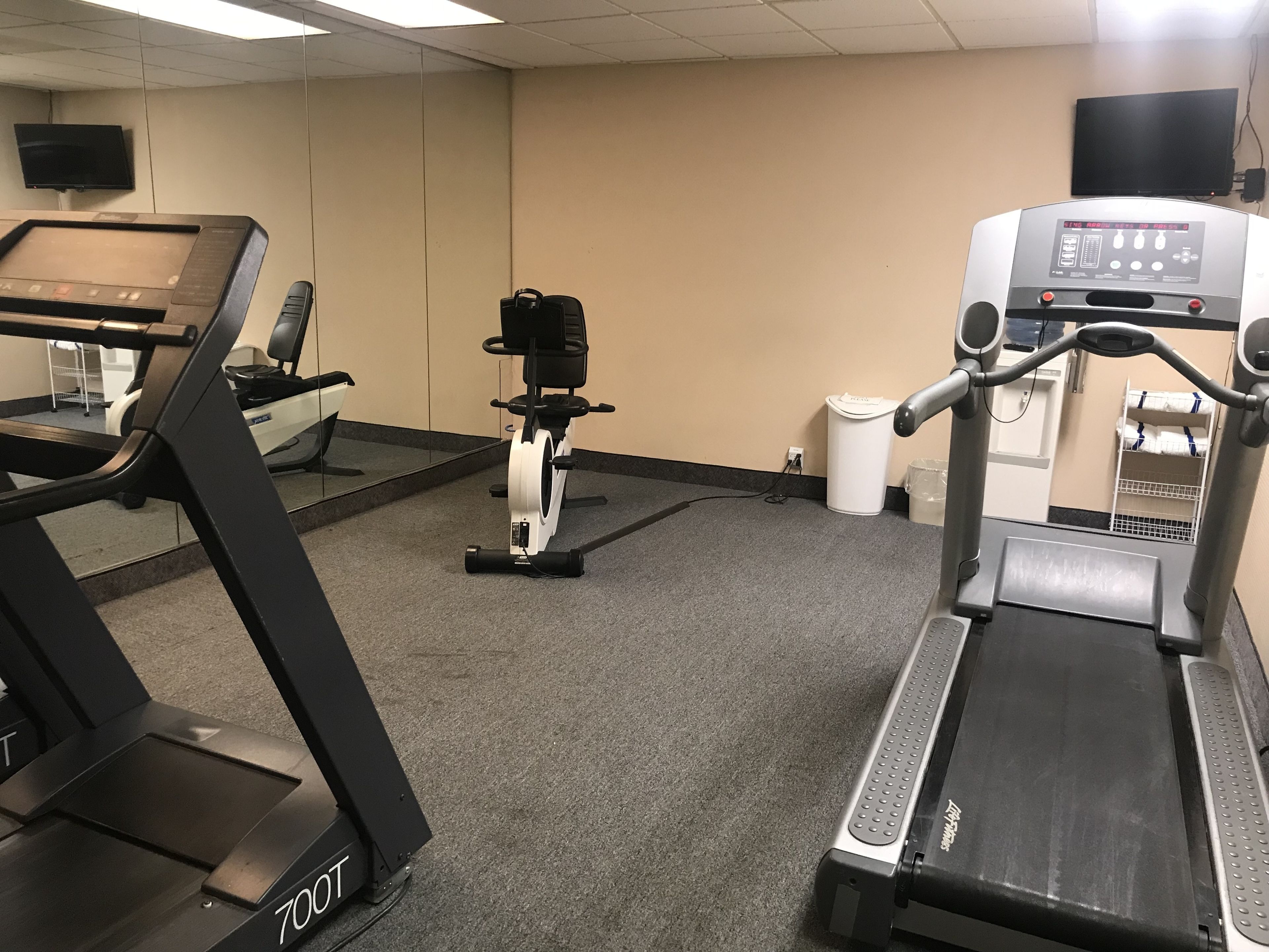 A gym with treadmills, stationary bikes, and a mirrored wall.